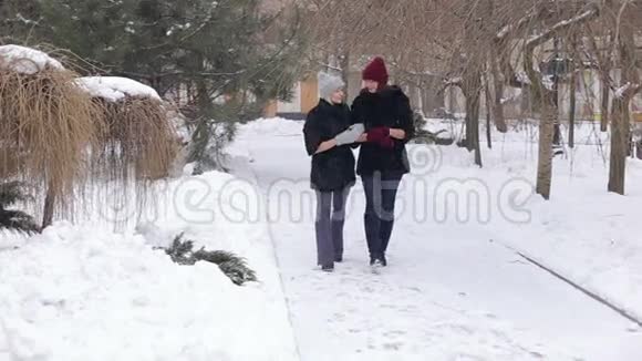 冬天两个穿着黑色毛皮大衣的漂亮女孩在公园里散步视频的预览图