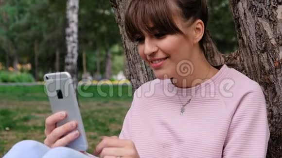 照片中年轻的白人女孩微笑着穿着粉色运动衫在智能手机上聊天视频的预览图