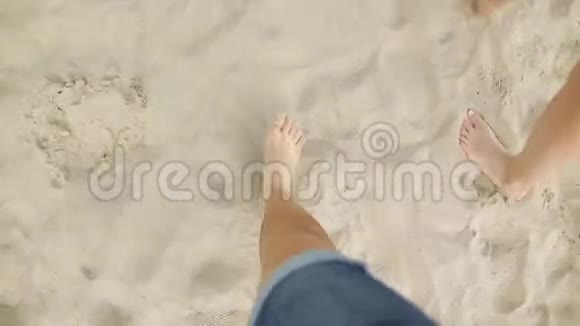 一对年轻夫妇在沙滩上踏着金色的沙滩在海洋附近行走的男性和女性腿视频的预览图