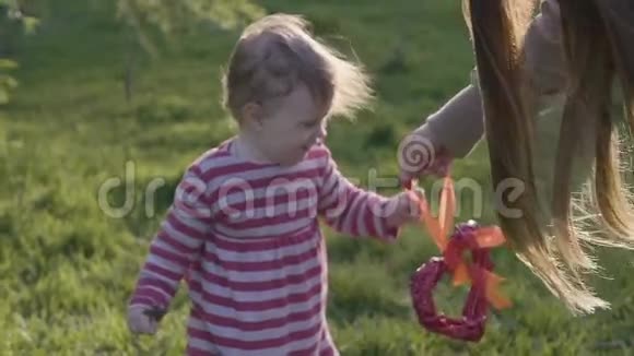 快乐的蹒跚学步的女孩走在草地上在春天的公园里从母亲那里拿走了一颗红色的复古心视频的预览图