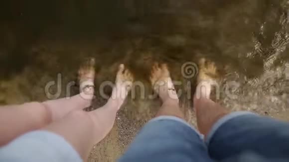 一对年轻夫妇的腿一起站在沙滩上的脏沙上光着脚站在里面视频的预览图