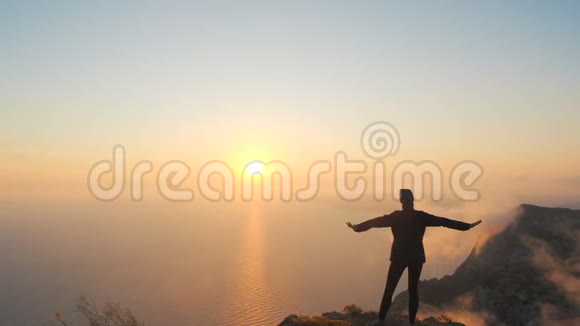 在克里米亚的一座高山上年轻女子伸出双臂在海面上观看一场美丽的戏剧性日落视频的预览图