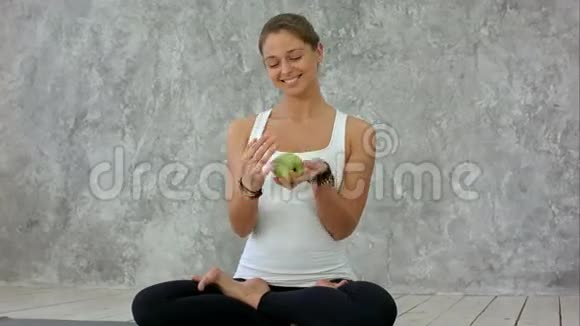 美丽的微笑的女人拿着绿苹果丛林与它坐在莲花的姿态视频的预览图