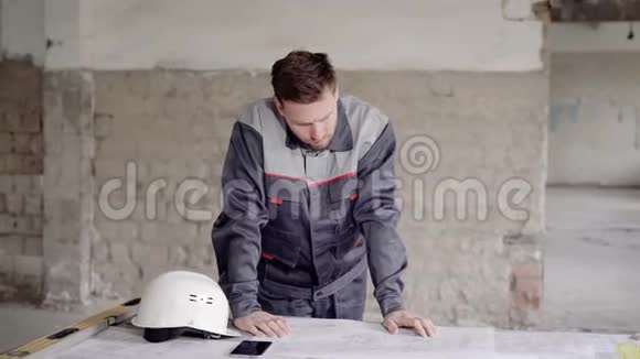 年轻工头穿着制服站在建筑工地上看着施工蓝图工人视频的预览图