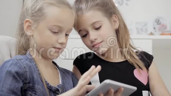 两个漂亮的小妹妹坐在一张桌子上玩平板电脑快乐的微笑女孩视频的预览图