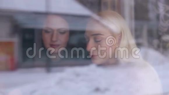 两个年轻女孩坐在咖啡馆里透过玻璃从街上眺望视频的预览图