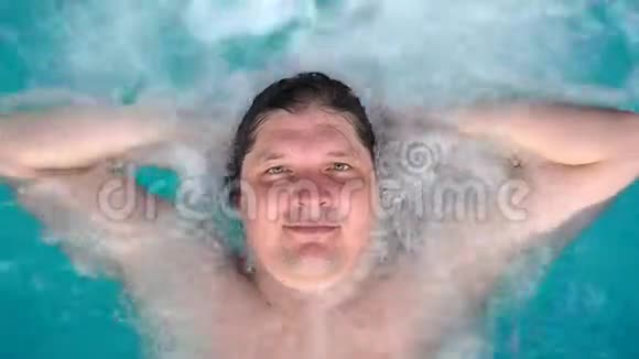 这个人躺在按摩浴缸里放松看着相机白种人躺在游泳池里躺在水里视图视频的预览图
