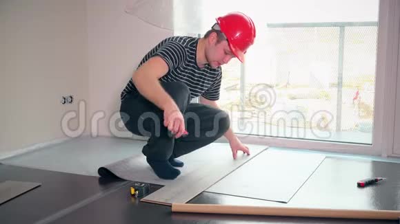 带红色头盔的熟练工人在新公寓里铺子垫视频的预览图