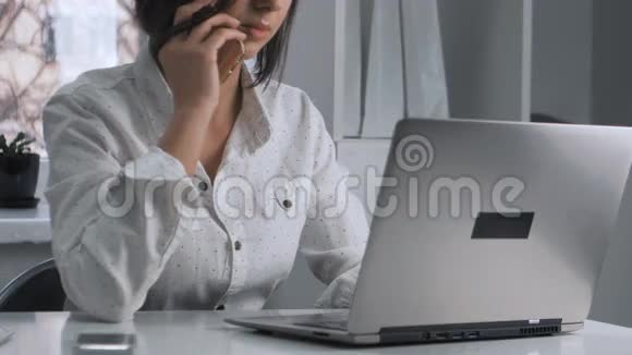 有魅力的商务女性会说手机在办公室的笔记本电脑上工作视频的预览图