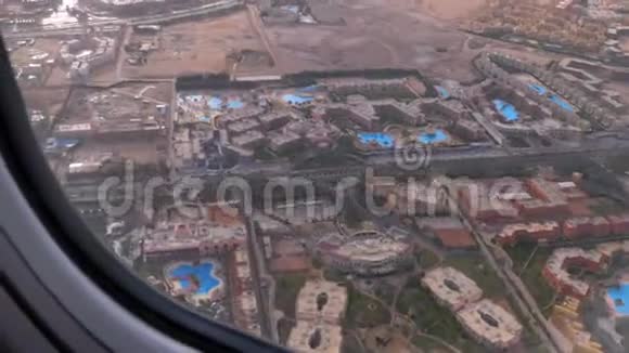 从热带度假胜地的飞机窗口可以看到埃及沙漠中的异国酒店和游泳池视频的预览图