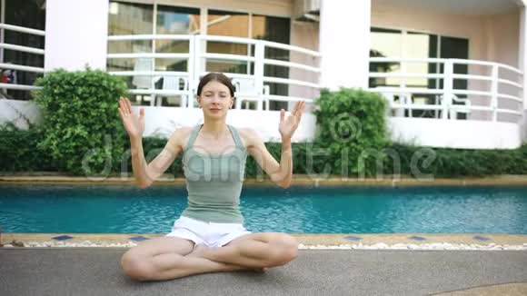 阳光明媚的一天在酒店附近的游泳池里做瑜伽的冷静的女人视频的预览图
