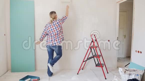年轻幸福的女人在新公寓画墙跳舞的慢镜头视频的预览图