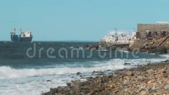 海浪拍打着海岸上的岩石背景上的货船视频的预览图