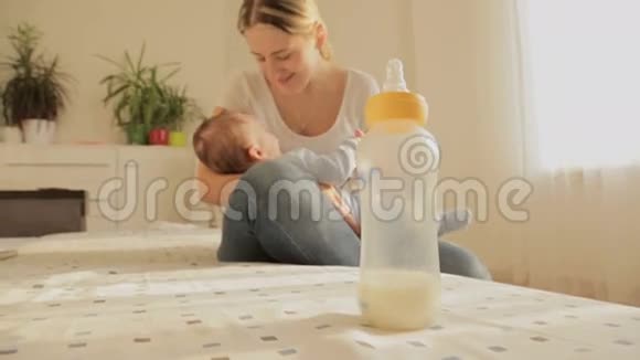 快乐的年轻母亲和她3个月大的小男孩坐在床上关注空瓶视频的预览图