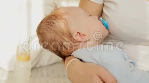 年轻母亲坐在床上摇着3个月大的小儿子的特写镜头视频的预览图