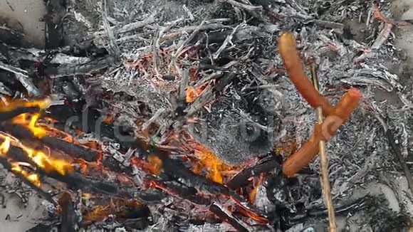 木棍上的两根香肠是在斯洛莫的篝火上炸的视频的预览图