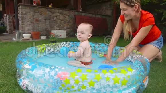快乐的年轻妈妈和一岁的小男孩一起在充气游泳池里泼水视频的预览图