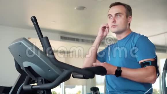 适合年轻人在健身房做运动的天鹅绒模拟器智能手机带耳机听音乐视频的预览图
