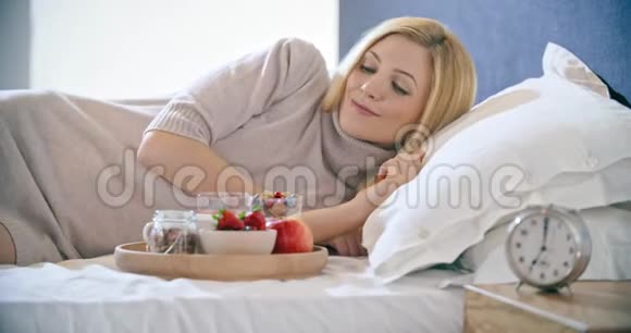 美丽的女人在床上吃早餐包括酸奶水果和谷类食品早上在卧室的家醒来高加索人视频的预览图