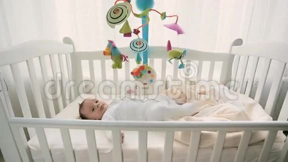 3个月大的可爱宝宝躺在床上看着玩具旋转木马视频的预览图