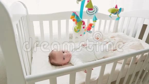 可爱的3个月男婴躺在婴儿床上看着玩具旋转木马视频的预览图