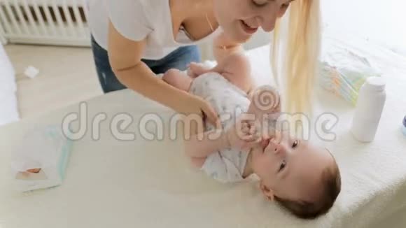 快乐的年轻妈妈一边说一边亲吻她3个月大的婴儿一边躺在换洗的桌子上视频的预览图