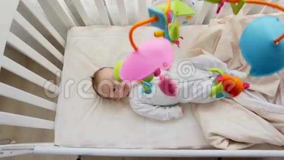 从上面看到可爱的3个月大的婴儿躺在婴儿床上看着旋转的彩色玩具旋转木马视频的预览图