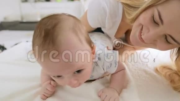特写镜头快乐的年轻妈妈玩着她3个月大的小男孩在床上爬行特写镜头可爱的3个月大的小宝宝博视频的预览图