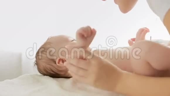 美丽的年轻母亲亲吻她3个月大的男孩躺在大窗户前换好的桌子上视频的预览图