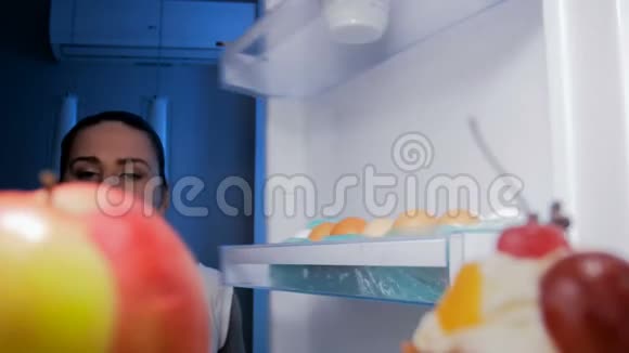 饥饿的女人晚上从冰箱里拿红苹果的4k镜头视频的预览图