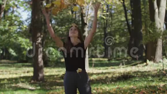 女孩捂着脸在秋天公园里挥舞着一根带着黄叶的枫树枝慢动作视频的预览图