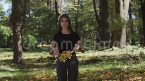 女孩捂着脸在秋天公园里挥舞着一根带着黄叶的枫树枝慢动作视频的预览图