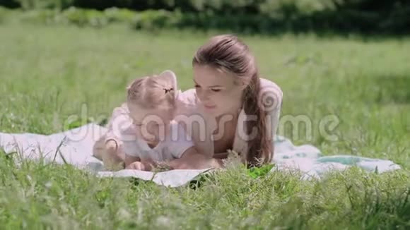 年轻的母亲和女儿在公园躺在草地上看书视频的预览图