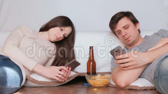 一对夫妇在手机上浏览互联网喝啤酒吃薯片视频的预览图