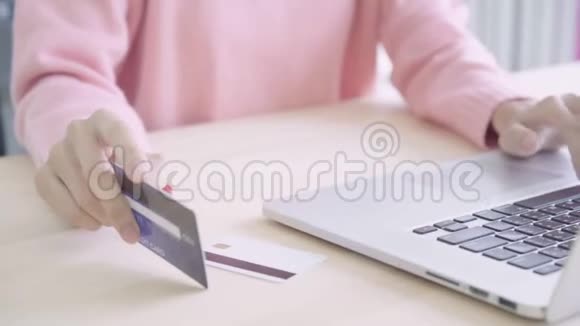 美丽的亚洲女人用电脑或笔记本电脑通过信用卡购买网上购物而穿毛衣坐在桌子上视频的预览图