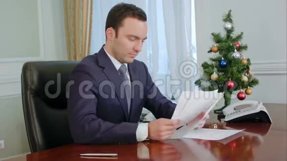 年轻商人在新年树附近的书桌旁阅读文件并签名视频的预览图