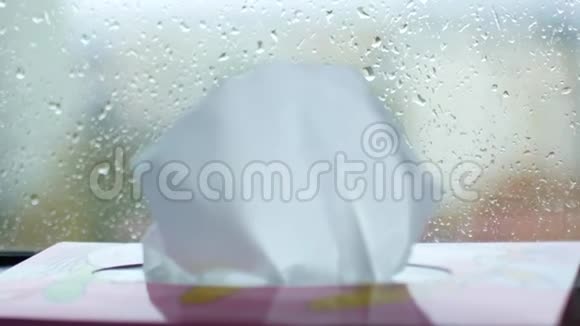 一个女人手把餐巾纸从盒子里拿出来箱子站在窗台上窗外下雨视频的预览图