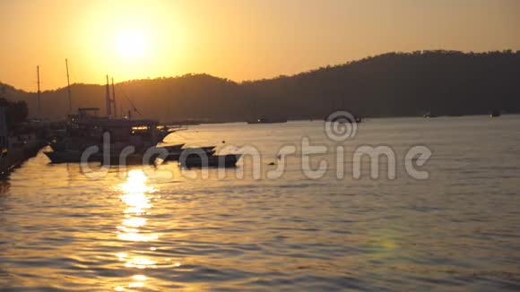 日落时分在海滨附近的渔船剪影在美丽的夜晚渔人的船只在海浪中摇曳视频的预览图