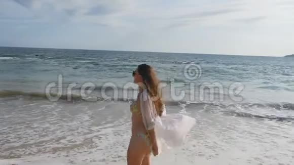 快乐的女人穿着比基尼和衬衫在海边散步举起手年轻漂亮的女孩享受生活视频的预览图
