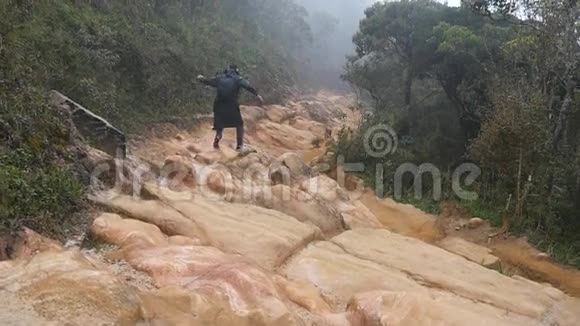 穿着雨衣的年轻人在旅途中在岩石小径上跳跃和慢跑徒步旅行者背着背包在石头地上奔跑视频的预览图