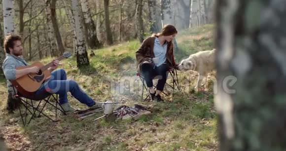 男人弹吉他女人一起在火地里抚摸狗真正的朋友户外露营帐篷度假视频的预览图