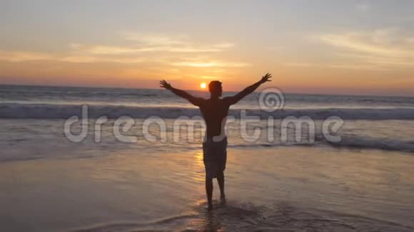 日落时分年轻人在海滩上的海水中散步举起双手运动员站在海边放松视频的预览图