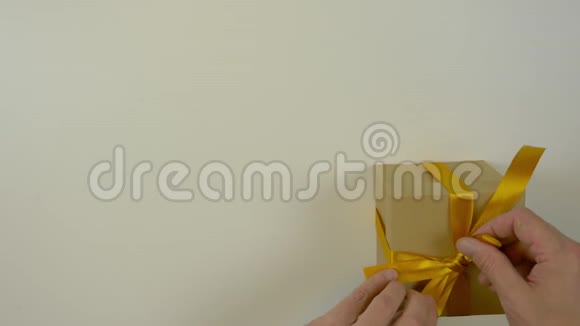 文字空间关闭顶部视图高角度男士双手从礼品盒上的缎带上拉直金蝴蝶结视频的预览图