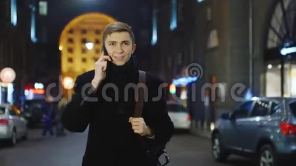 那个年轻人晚上在城里散步用手机说话视频的预览图