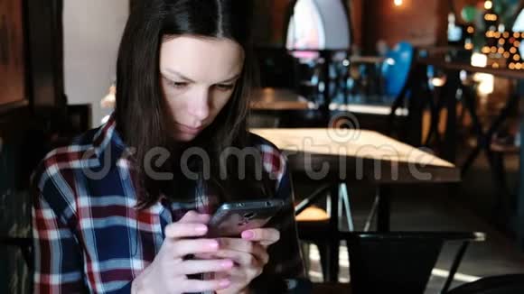 坐在咖啡馆里的女人在电话里发信息或使用互联网穿着格子衬衫视频的预览图