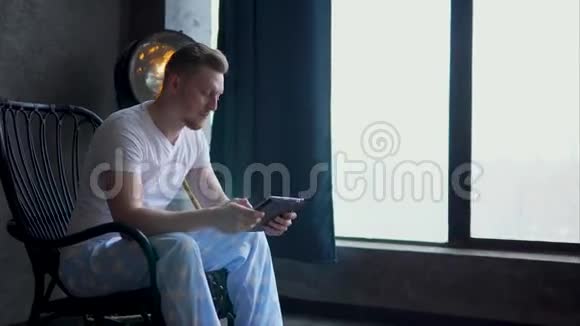 一个坐在木椅上的年轻人在便携式平板电脑上工作视频的预览图
