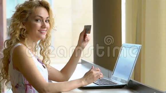 美丽的女人手里拿着信用卡用手提电脑键盘输入安全密码视频的预览图