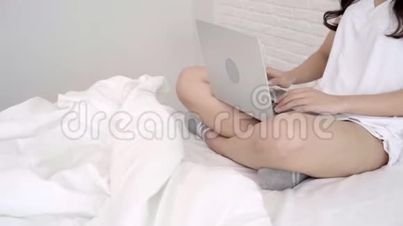 美丽的亚洲女人在卧室里躺在床上玩电脑或笔记本电脑视频的预览图