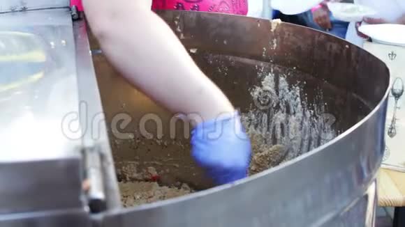 一个女人手把粥从一个大缸里倒进一个塑料盘子里街头美食快餐街头小吃美味视频的预览图