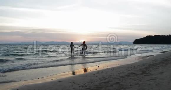 在蜜月假期中一对夫妇在夕阳下的沙滩上牵手幸福的男人和女人视频的预览图